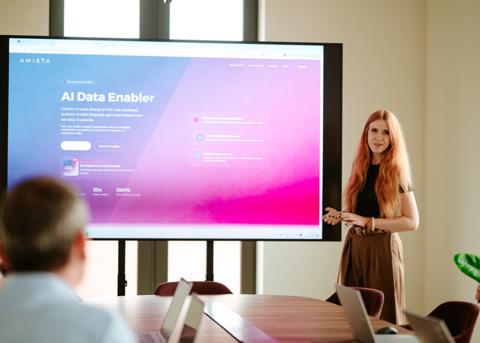 Woman presenting an AI Data Enabler on a screen in a meeting room, with attendees seated around a conference table.