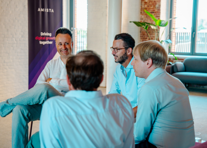 Four men sit in a discussion, with a banner in the background promoting digital growth, in a bright workspace.