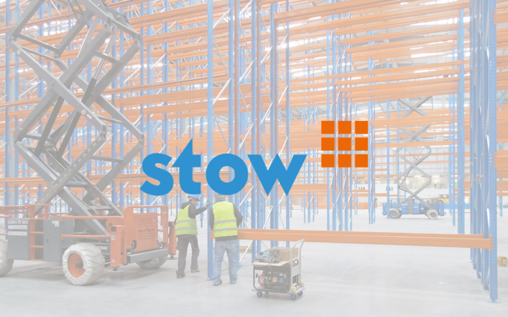 Warehouse interior with empty blue and orange storage racks, two workers in vests, and scissor lifts.